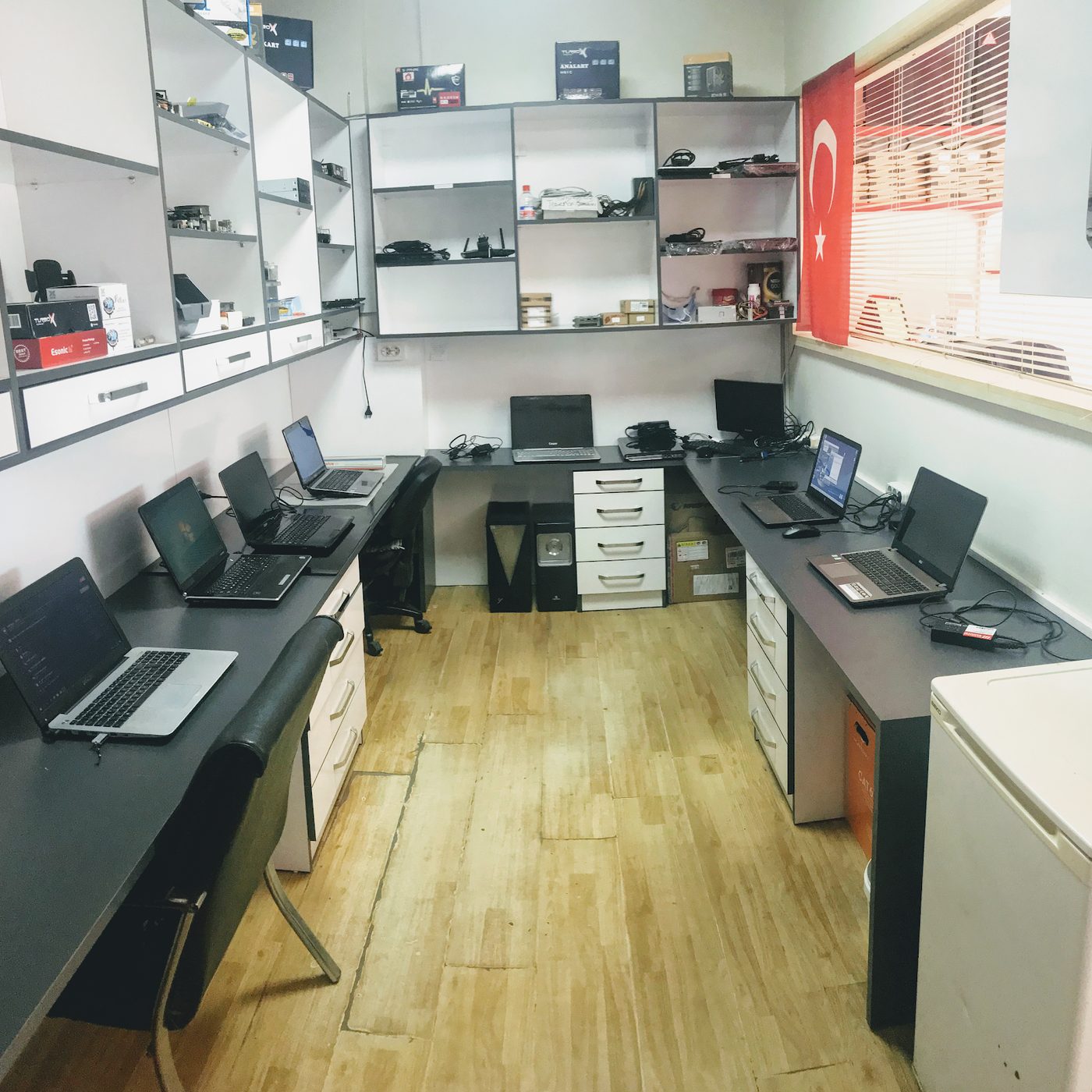 Ostim'deki atölyemizin servis masaları; test için sıraya dizilmiş açık laptoplar ve raflarda yedek parçalar