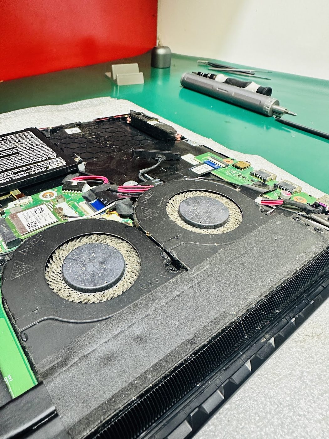 Alt kapağı açılmış bir laptopta tozla tıkanmış çift fan ve bakır soğutucu kanatları, temizlik öncesi
